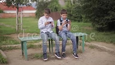 两个男孩坐在长凳上玩网络<strong>游戏</strong>。 一个带<strong>背包</strong>的男孩。 年轻人用电话